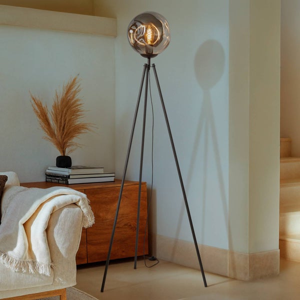 Dekorative Stehlampe mit Stativbeinen und runder Glaskugel im Wohnraum.