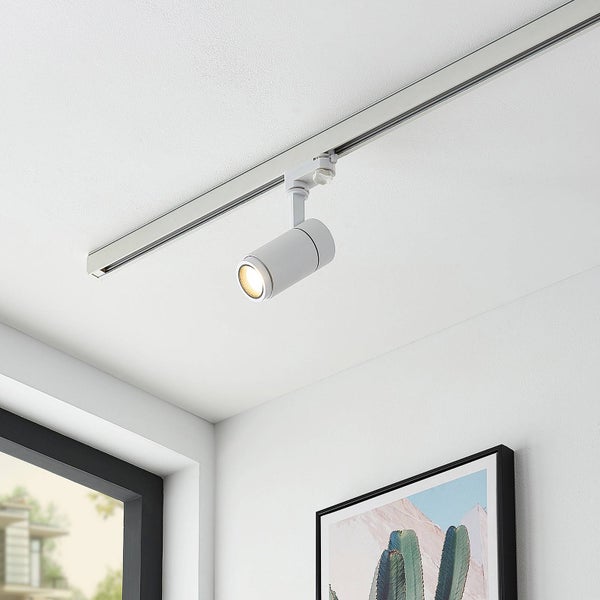 Weißer zylindrischer Schienenstrahler an einer schmalen Deckenschiene in einem hellen Raum mit einem Bild an der Wand.