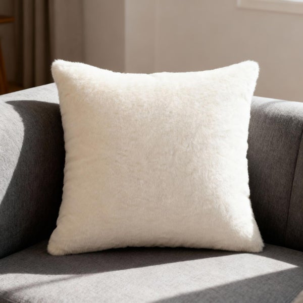 Weiches, weißes Dekokissen in Felloptik auf einem grauen Sofa.