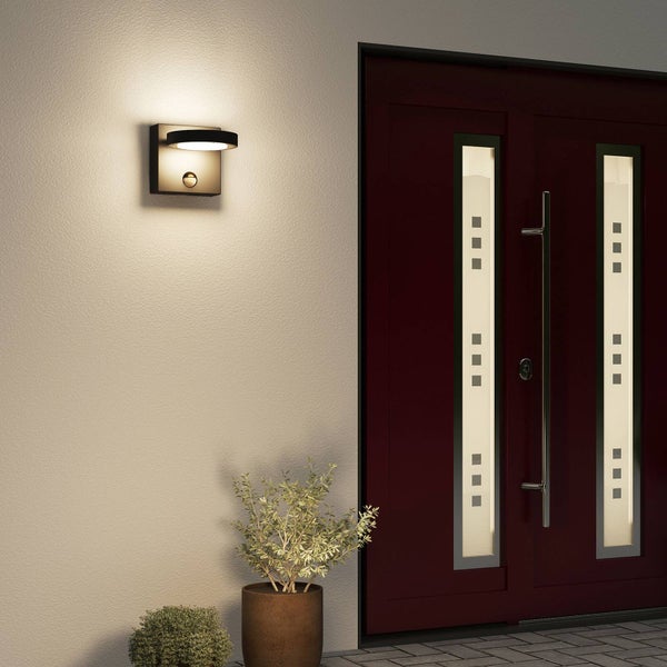 Moderne Außenwandleuchte mit Bewegungsmelder an einer Hauswand neben einer Eingangstür montiert, stimmungsvolle Beleuchtung.