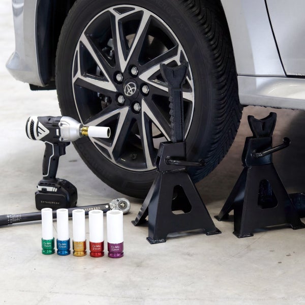 Autowerkzeug-Set mit Schlagschrauber, Drehmomentschlüssel, bunten Kraft-Steckschlüsseleinsätzen und zwei Unterstellböcken neben einem Autoreifen.
