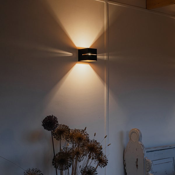 Quadratische Wandleuchte an einer Wand mit Blumenstrauß davor