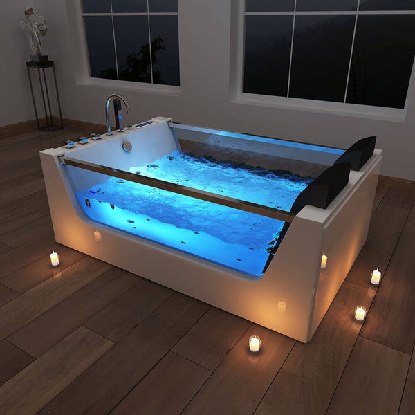 Moderne Whirlpool Badewanne mit Glasfront und blauer Unterwasserbeleuchtung in einem Badezimmer mit Holzboden und Kerzen.