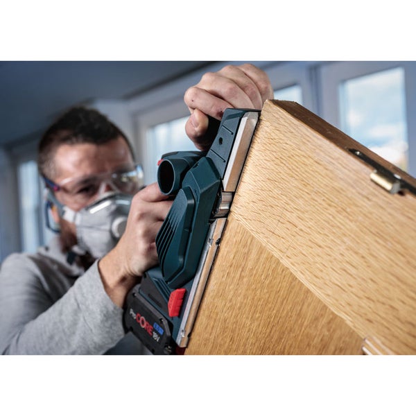 Ein Mann hobelt ein Holzbrett mit einem Elektrohobel.