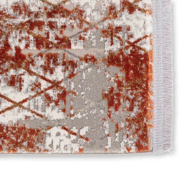 Detail eines gewebten Kurzflorteppichs mit abstraktem Muster in Rostrot und Grau sowie Fransen an der Abschlusskante.