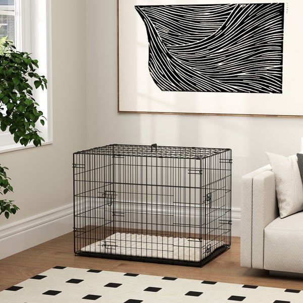 Hundekäfig aus schwarzem Metalldraht mit heller Matte in einem hellen, modern eingerichteten Wohnzimmer neben einem Sofa.