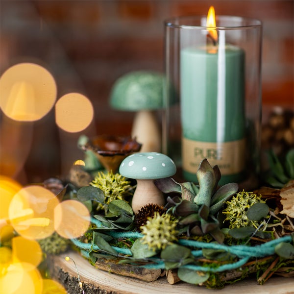 Dekorative Anordnung mit Kerze im Glas, Holzpilzen und Pflanzen auf einem Holztablett