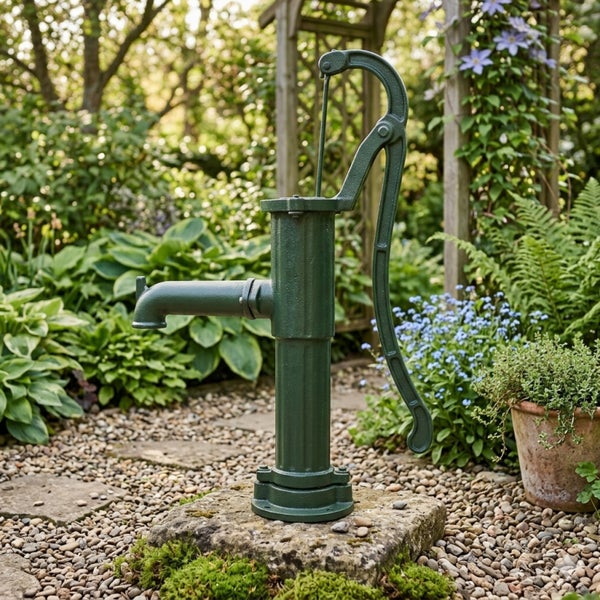 Nostalgische Schwengelpumpe aus Gusseisen in einem bepflanzten Garten auf einem Naturstein.