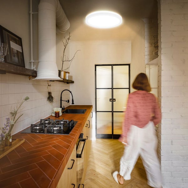 Runde LED-Deckenleuchte beleuchtet moderne Küche mit terracottafarbener Arbeitsplatte, hellem Fischgrätparkett und weißer Dunstabzugshaube.