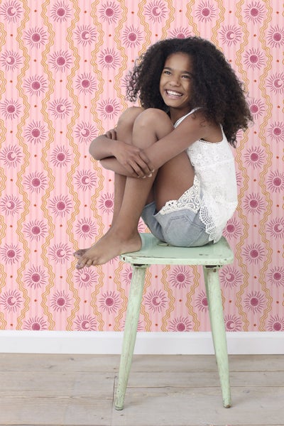 Mädchen sitzt auf einem Hocker vor einer Wand mit Sonnen- und Mondtapete