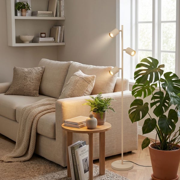 Moderne Stehleuchte mit drei verstellbaren Leuchtköpfen in einem hell eingerichteten Wohnzimmer neben einem Sofa und einem Beistelltisch.