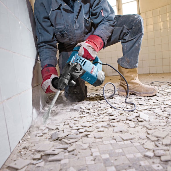 Handwerker entfernt Bodenfliesen mit einem Bosch Bohrhammer und Flachmeißel in einem gefliesten Raum.