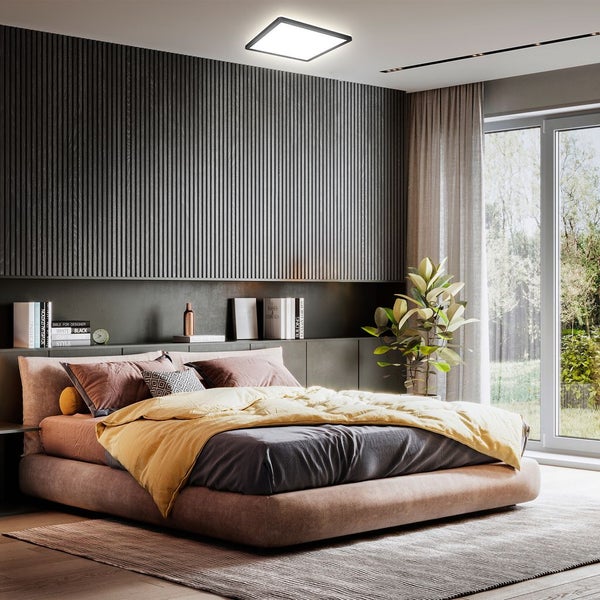 Schlafzimmer mit Bett, Nachttisch und Zimmerpflanze unter einer Deckenleuchte