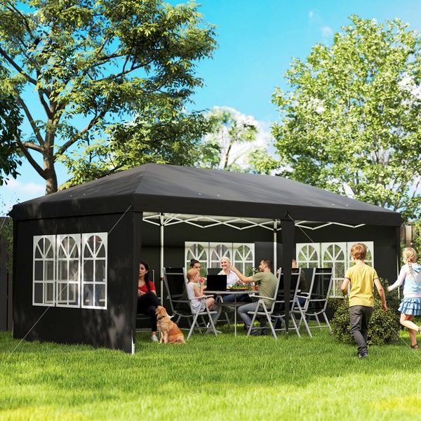 Schwarzer Faltpavillon mit Seitenwänden und Bogenfenstern im Garten, Menschen sitzen im Inneren, Kinder spielen auf dem hellen Rasen.