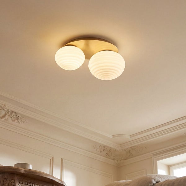 Moderne Deckenleuchte mit zwei geriffelten Glaskugeln auf einer messingfarbenen Metallbasis in einem hellen Raum mit Wandleisten.