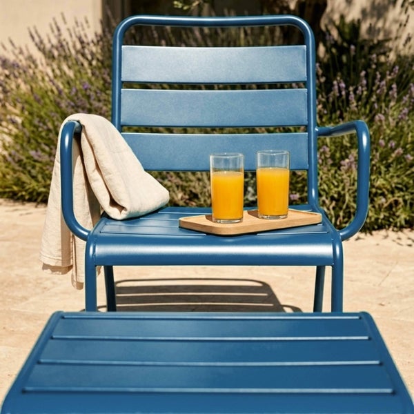 Blauer Garten-Lounge-Sessel aus Metall mit Lamellen, Armlehnen und Beistelltisch in einer hellen Gartenumgebung mit Lavendel.