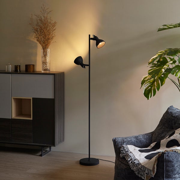 Modernes Wohnzimmer mit einer schwarzen zweiflammigen Stehleuchte, einem Sideboard, einer großen Zimmerpflanze und einem grauen Sessel.