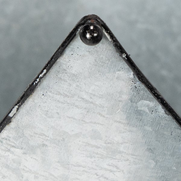 Nahaufnahme einer Ecke eines verzinkten Metalltabletts mit Metallrahmen und dekorativer Metallkugel an der Spitze.