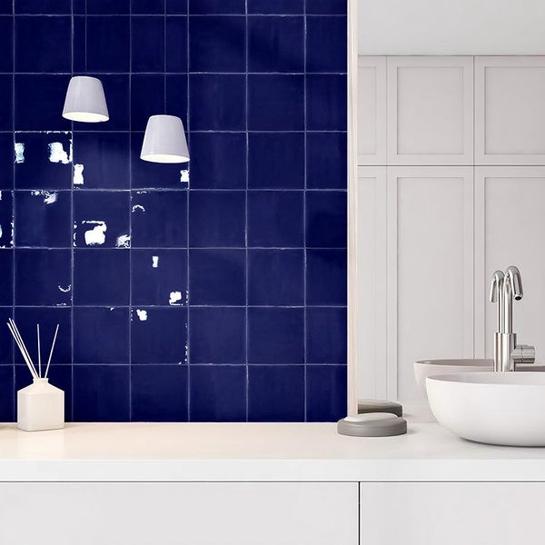 Badezimmer mit quadratischen glänzenden Wandfliesen in einem Waschtischbereich mit einem runden Aufsatzwaschbecken und einer Armatur.