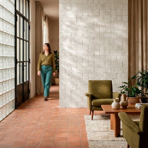 Wohnraum mit quadratischen Wandfliesen, Terrakottaboden und Sesseln in einem modernen, hellen Innenraum mit Glasbausteinen.
