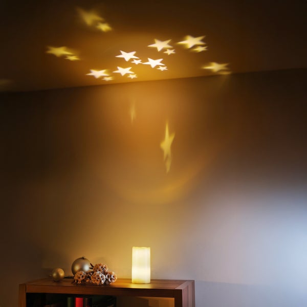Dekorative Lampe projiziert Sterne an Wand und Decke, aufgestellt auf einem Regal mit Weihnachtsdekoration.