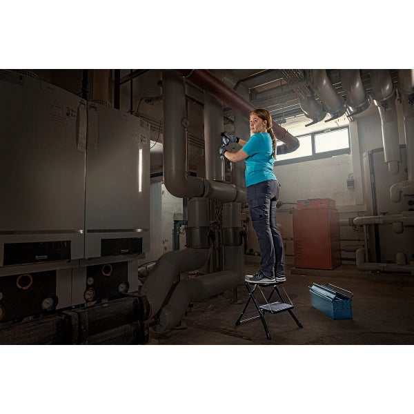 Frau steht auf einem Tritt und arbeitet an Rohren in einem Heizungskeller.