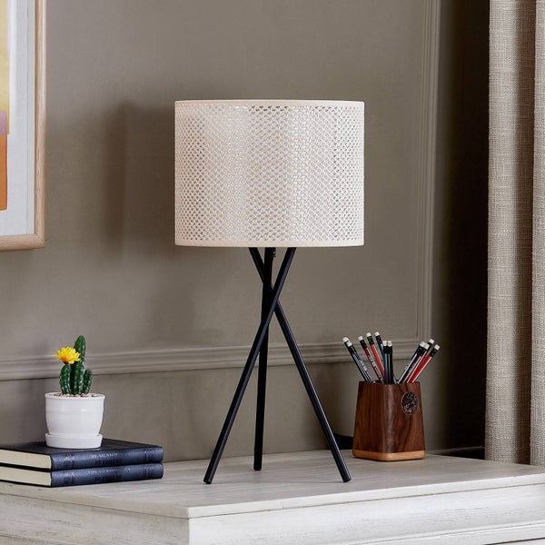 Tischleuchte mit schwarzem Dreibein-Gestell und gewebtem Schirm auf einem hellen Holztisch neben einem Kaktus und einem Stifteköcher.