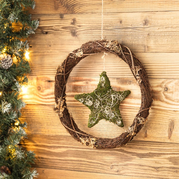 Hängender Weihnachtskranz aus Reben mit einem moosbedeckten Stern in der Mitte vor einer rustikalen Holzwand.
