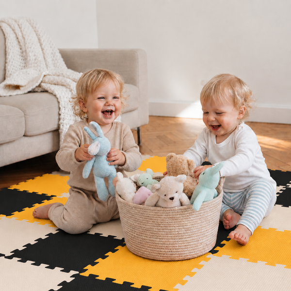 Zwei Kleinkinder spielen mit Stofftieren in einem geflochtenen Korb auf einer Puzzlematte im Wohnzimmer.