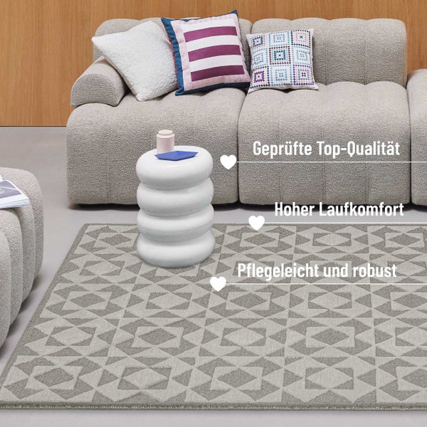 Modernes Wohnzimmer mit grauem geometrisch gemustertem Teppich, hellem strukturiertem Sofa mit Kissen und weißem Beistelltisch.
