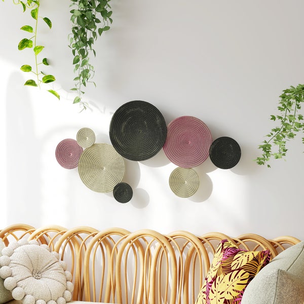Dekorative Wandgestaltung mit runden Textilbildern über einem Rattansofa mit Kissen