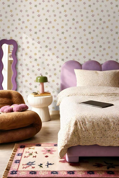 Einrichtung eines Kinderzimmers mit Vliestapete mit Blumenmuster an der Wand, kombiniert mit einem Polsterbett, einem Sessel und einem Teppich.