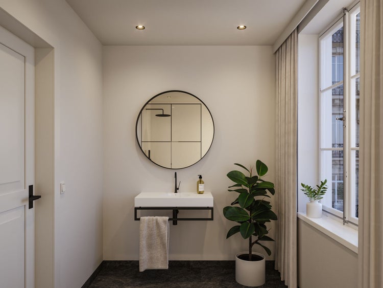Modernes, helles Badezimmer mit weißem Waschbecken, schwarzer Armatur, rundem Spiegel, großer Zimmerpflanze und Fenster mit Vorhang.