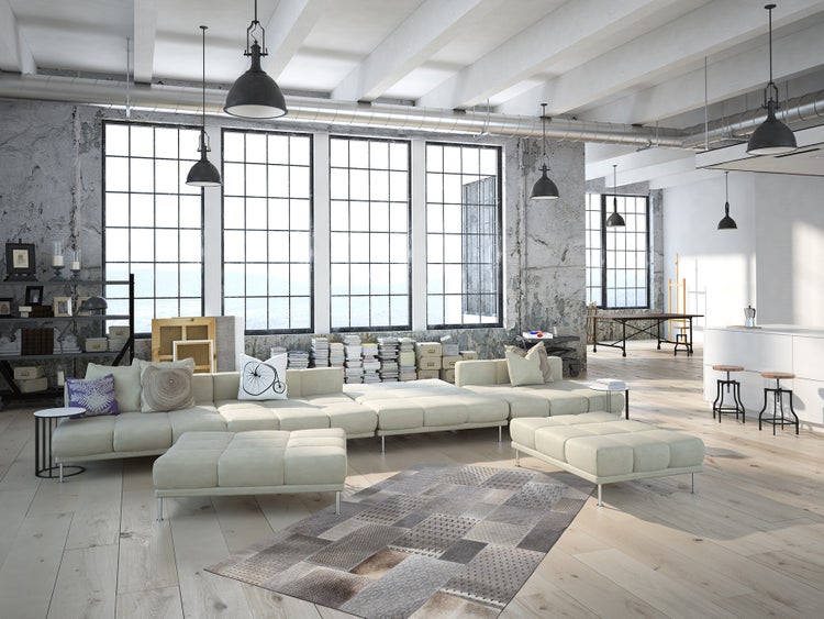 Großes, offenes Loft im Industriestil mit hohen Decken, großen Sprossenfenstern, Betonwänden, Holzboden und modernem Sofa mit zwei Hockern.