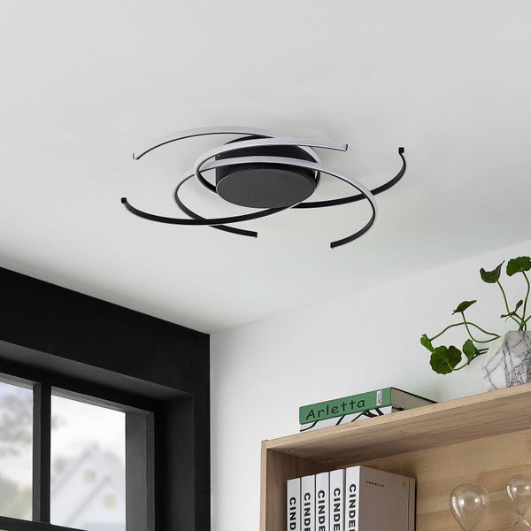 Moderne LED-Deckenleuchte mit geschwungenen schwarzen und weißen Lichtbändern an der Decke über einem Bücherregal.