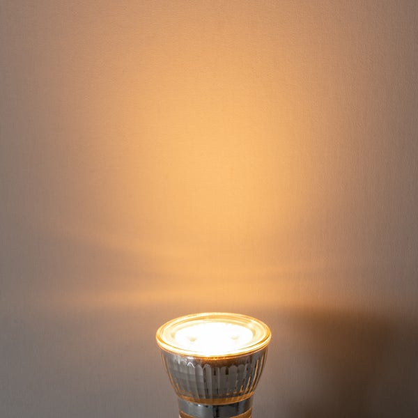 Eingeschaltete LED-Reflektorlampe GU10 mit warmweißem Lichtkegel an einer Wand.