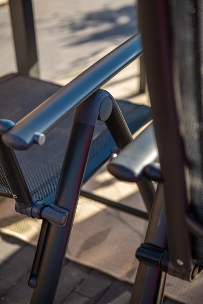 Detailaufnahme der Armlehne und des Klappmechanismus eines Gartenstuhls aus Metall mit Netzbespannung.