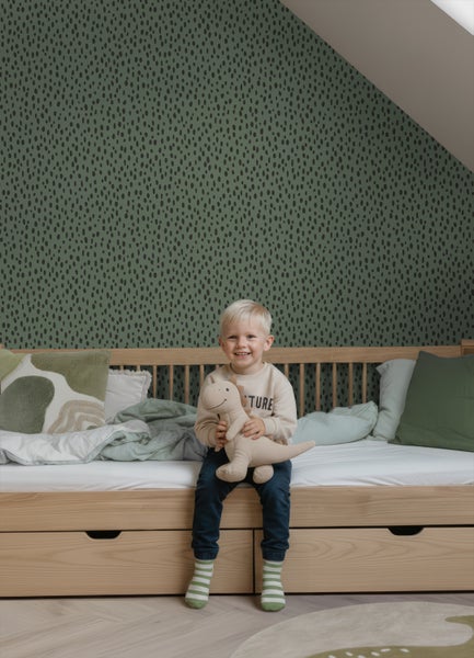 Vliestapete mit grünem Pünktchenmuster in einem hellen Kinderzimmer mit Holzbett und Kissen.