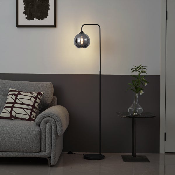 Moderne Stehleuchte aus schwarzem Metall mit einer Glaskugel im Wohnzimmer neben einem grauen Sofa und Beistelltisch.