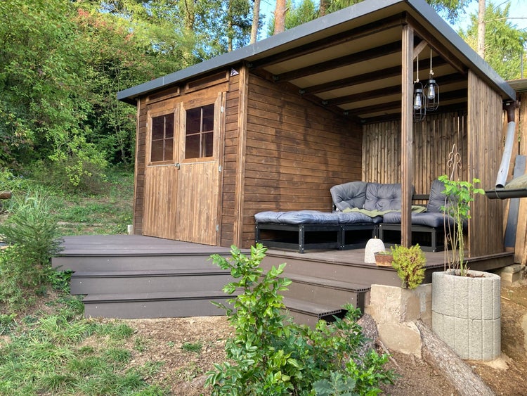 Gartenhaus aus Holz mit Pultdach, Doppeltür und integrierter Terrasse mit Lounge-Sitzgruppe und Treppenstufen.
