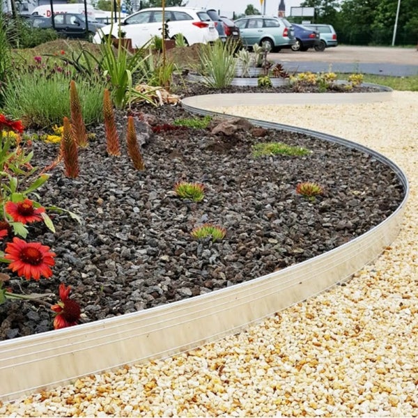 Flexible Rasenkante aus Metall zur Trennung von einem Pflanzbeet mit dunklem Lavamulch und einem hellen Kiesweg.