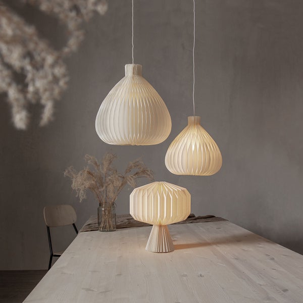 Szene mit zwei Hängeleuchten und einer Tischleuchte aus Papier auf einem Holztisch.