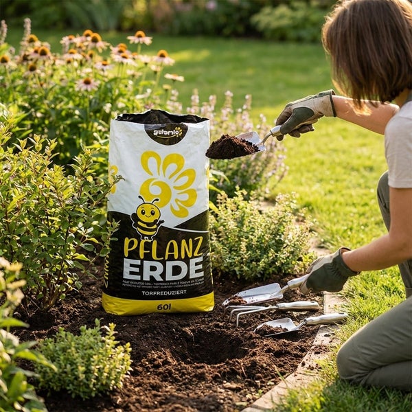 Eine Person gärtnert in einem sonnigen Blumenbeet mit einem 60 Liter Sack torfreduzierter Pflanzerde von galanlo und verschiedenen Gartenwerkzeugen.