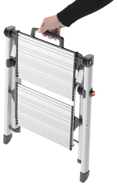 Zusammengeklappte Aluminium Trittstufe mit Tragegriff wird von einer Hand gehalten.