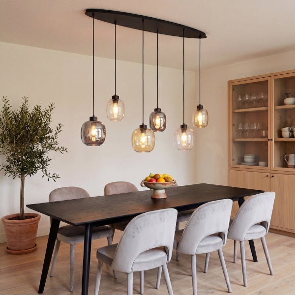 Modernes Esszimmer mit sechs-flammiger Pendelleuchte über dunklem Holztisch, grauen Polsterstühlen, Olivenbaum im Topf und hellem Holzschrank.