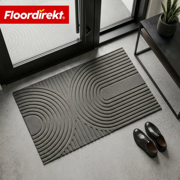 Floordirekt Logo. Moderne strukturierte Fußmatte mit geometrischem Bogenmuster auf einem Betonboden im Eingangsbereich vor einer Glastür.