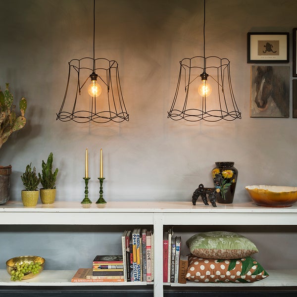Zwei schwarze Pendelleuchten mit Drahtschirm über einer weißen Konsole mit Büchern, Pflanzen und Dekoration.