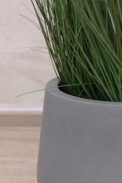Nahaufnahme von künstlichem Gras in einem grauen Pflanzgefäß mit matter Oberfläche.