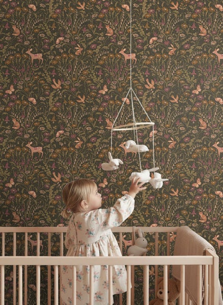 Tapete mit Waldtieren und Blumenmuster in einem Kinderzimmer mit Kind im Gitterbett.