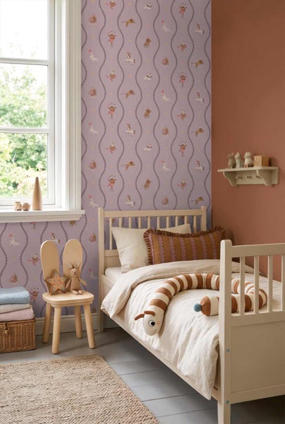 Helles Kinderzimmer mit Vliestapete im Zirkusdesign, einem Holzbett und einem Stuhl mit Hasenohren vor einem terracottafarbenen Wandabschnitt.